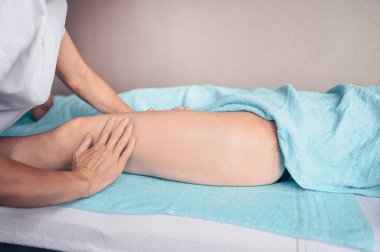 Masaj masasında uzanmış terapi masajından zevk alan tanınmayan genç bir kadın. Vücut bakımı, kilo verme konsepti. El masajı terapisti spa kliniğinde anti-selülit masaj yapıyor.