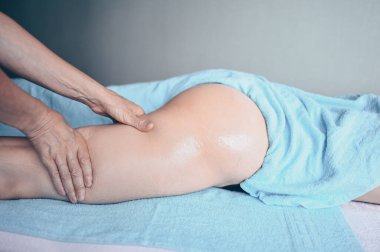 Masaj masasında uzanmış terapi masajından zevk alan tanınmayan genç bir kadın. Vücut bakımı, kilo verme konsepti. El masajı terapisti spa kliniğinde anti-selülit masaj yapıyor.