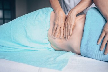 Masaj masasında uzanmış terapi masajından zevk alan tanınmayan genç bir kadın. Vücut bakımı, kilo verme konsepti. El masajı terapisti spa kliniğinde anti-selülit masaj yapıyor.