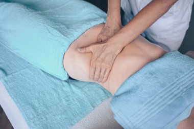 Masaj masasında uzanmış terapi masajından zevk alan tanınmayan genç bir kadın. Vücut bakımı, kilo verme konsepti. El masajı terapisti spa kliniğinde anti-selülit masaj yapıyor.
