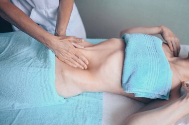 Masaj masasında uzanmış terapi masajından zevk alan tanınmayan genç bir kadın. Vücut bakımı, kilo verme konsepti. El masajı terapisti spa kliniğinde anti-selülit masaj yapıyor.