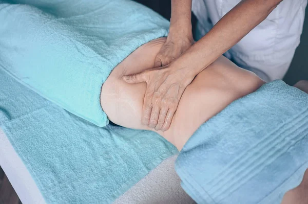 Masaj masasında uzanmış terapi masajından zevk alan tanınmayan genç bir kadın. Vücut bakımı, kilo verme konsepti. El masajı terapisti spa kliniğinde anti-selülit masaj yapıyor.