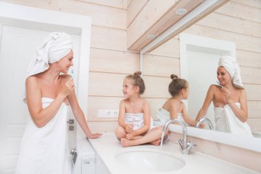 Dişlerini fırçalayan ve birlikte vakit geçiren mutlu bir aile. Anne ve kızı beyaz banyoda öpüşüp sarılıyorlar. Kafalarında ve vücutlarında havlular olan kadın ve kız. 