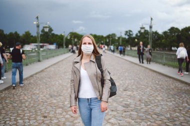 Covid 19 önleme için yüz koruyucu maske takmış genç sarışın bir kadın. Sırt çantalı beyaz öğrenci ya da gezgin turist. Corona virüsü konsepti.