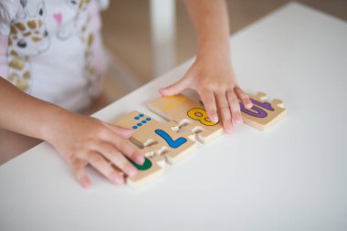 Anaokulunda masa başında otururken okul için hazırlanan, ahşap matematiksel çok renkli figürlerle eğitim oyunları oynayan anaokulu çocuğu elleri. Okul konseptine dönelim.
