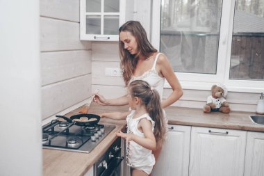 Mutlu aile kahvaltıya peynirli kek hazırlıyor. Güzel genç anne ve tatlı kızı mutfakta yemek pişiriyor ve eğleniyorlar. Küçük yardımcısıyla ev yapımı sağlıklı yiyecekler.