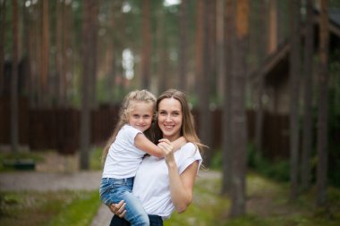 Mutlu gülümseyen annesi ve beyaz tişörtlü ve kot pantolonlu sevimli duygusal kızı kırsal alanda kucaklaşıp eğleniyorlar. Yazı ailemle geçiriyorum.