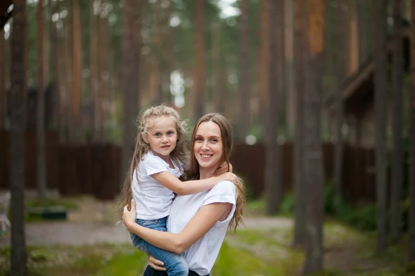 Happy smiling mother and her cute emotional little daughter child in white shirts and denim jeans are hugging and having fun outdoor in nature at countryside. Spending summer time with family