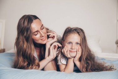 Mutlu ve sevgi dolu bir ailenin portresi yatak odasında uzanıp birlikte eğleniyor. Anne ve okul öncesi kızı pijamalı çocuk yatakta oynaşıp sarılıyorlar. Anneler günün kutlu olsun.