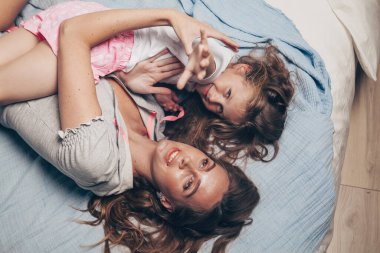 Mutlu sevgi dolu aile uzanıp yatak odasında birlikte eğleniyor. Anne ve kreş kızı pijamalı çocuk sabahın ilk ışıklarında yatakta oynaşıp sarılıyorlar. Anneler günün kutlu olsun.