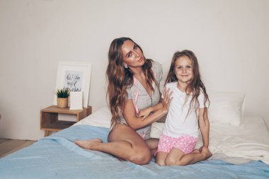 Mutlu sevgi dolu aile uzanıp yatak odasında birlikte eğleniyor. Anne ve kreş kızı pijamalarıyla sabahları yatakta oynaşıp sarılıyorlar. Anneler günün kutlu olsun.