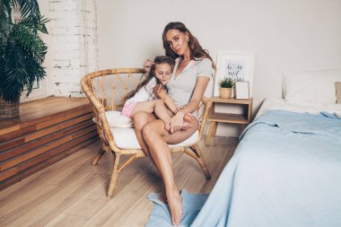 Mutlu sevgi dolu aile uzanıp yatak odasında birlikte eğleniyor. Anne ve kreş kızı pijamalı çocuk sabahın köründe hasır bir sandalyede oturuyorlar. Anneler günün kutlu olsun.