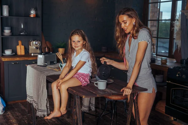 Happy loving family preparing dinner together. Smiling Mom and child daughter girl cooking and having fun in the kitchen. Homemade healthy food. Little helper in a dark kitchen interior at home.