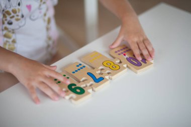 Anaokulunda masa başında otururken okul için hazırlanan, ahşap matematiksel çok renkli figürlerle eğitim oyunları oynayan anaokulu çocuğu elleri. Okul konseptine dönelim.