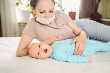 Koruyucu yüz maskesi takmış güzel bir anne kucağında yeni doğmuş oğlunu virüslerden ve enfeksiyonlardan koruyor. Coronavirus covid-19 önleme. Ev karantinası. Evde mutlu bir aile