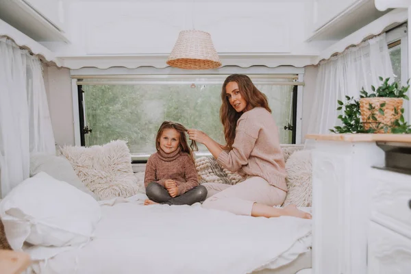 Ευτυχισμένη οικογένεια - μητέρα και μικρή κόρη χαλαρώνουν αγκαλιάζοντας και διασκεδάζοντας στην ύπαιθρο μέσα σε λευκό σκανδιναβικό ρουστίκ τροχόσπιτο στο εσωτερικό. Έννοια εγχώριου τουρισμού. — Φωτογραφία Αρχείου