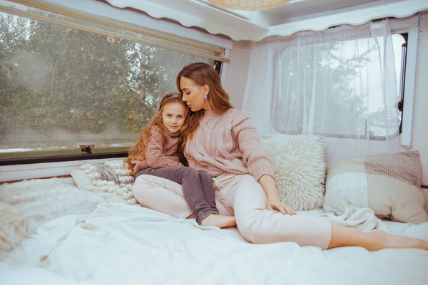 Ευτυχισμένη οικογένεια - μητέρα και μικρή κόρη χαλαρώνουν αγκαλιάζοντας και διασκεδάζοντας στην ύπαιθρο μέσα σε λευκό σκανδιναβικό ρουστίκ τροχόσπιτο στο εσωτερικό. Έννοια εγχώριου τουρισμού. — Φωτογραφία Αρχείου