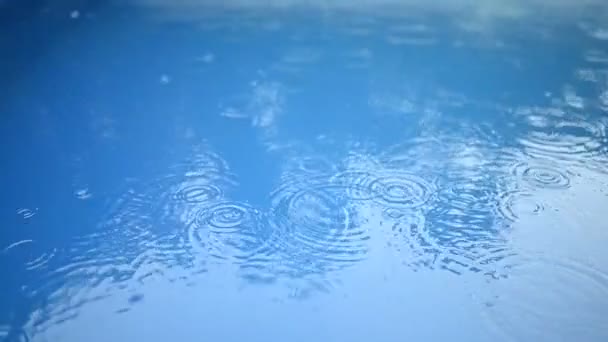 Cirkels van regendruppels op het oppervlak van het blauwe water. Abstracte achtergrond. Regen in het zwembad. — Stockvideo