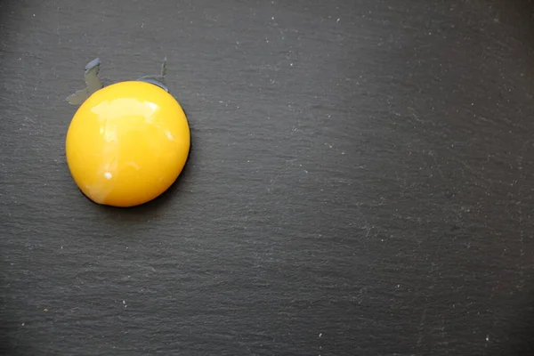 the yolk of a chicken egg or half a peach lies in a corner on the side on a gray stone black background with space for text