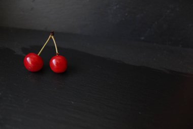 İki kiraz, yiyecek için gri taştan siyah bir zemin üzerinde yatıyor.