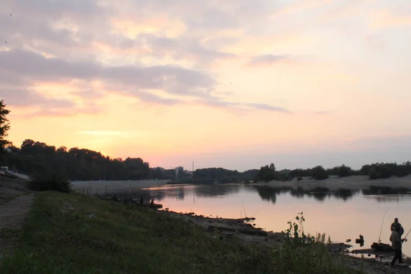川の向こうにピンク色の暖かい風景の夕日が立っていて釣りをしている — ストック写真