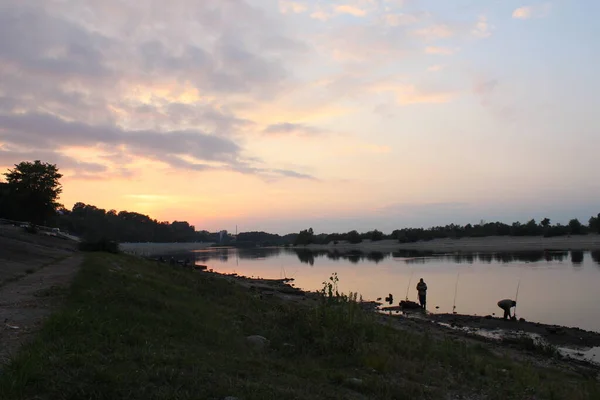 川の向こうにピンク色の暖かい風景の夕日が立っていて釣りをしている — ストック写真