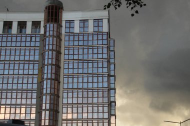 Bina, günbatımında güneş tarafından aydınlatılan bulutlarla birlikte mavi gökyüzünün arka planında cam cepheli modern bir yerleşim tesisidir.