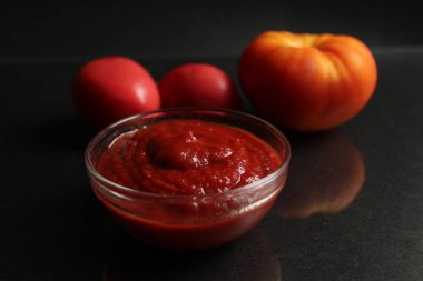 Kırmızı domates soslu bir cam tencere arka planda sebze domatesleri kırmızı turuncu domatesler ve Kopi uzaylı sarı kabuklu soğanların yanında duruyor.
