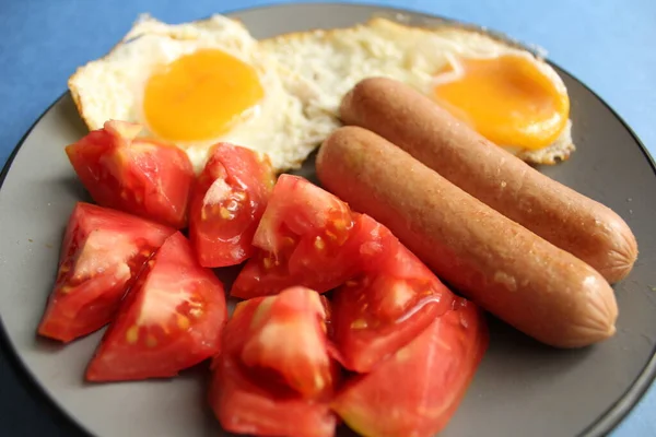 传统的欧洲早餐鸡蛋香肠和沙拉蔬菜红色西红柿放在蓝色底盘上 有复制空间 — 图库照片