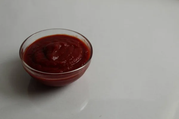 赤いトマトのホットソースか甘いソースが白い灰色の背景のコピースペースにガラスの鍋皿に注がれます — ストック写真