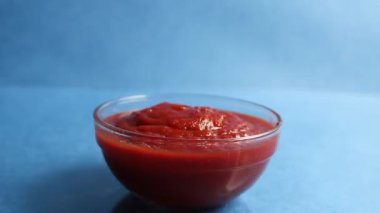 Kaşık kadranları cam tencere kırmızı domates sosundan mavi arka planda pişirilen yemeklerden alır.