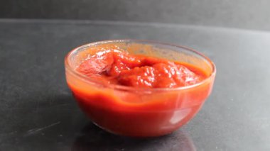 Kırmızı domates sosu mavi arka planda cam bir tencere üzerine dökülüyor.