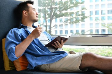 Elinde kitapla evde kanepede otururken içme kahve genç adam 