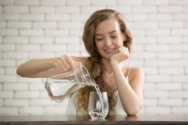 若い女性の部屋のガラスに水差しから水を注ぐ — ストック写真