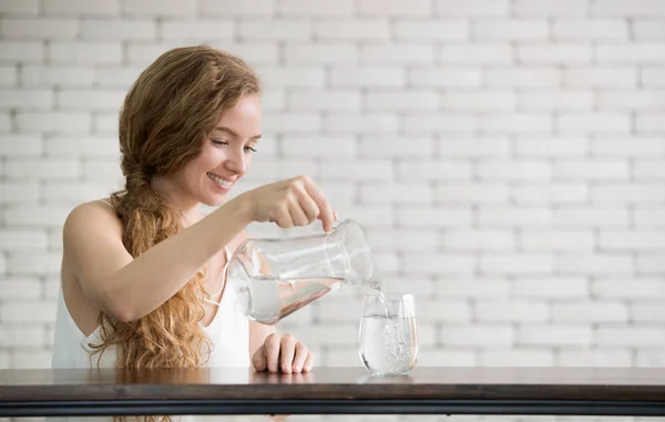 若い女性の部屋のガラスに水差しから水を注ぐ — ストック写真