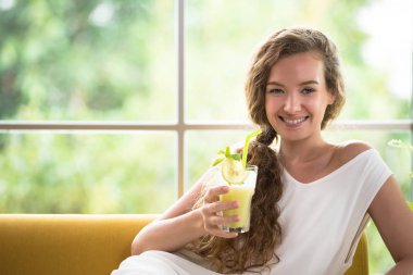 Rahat ve konforlu bir bardak meyve suyu seyir tutan bir kanepede yatan sağlıklı genç kadın