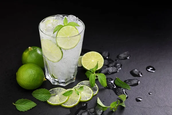 Fresh lime soda in glass drink with sliced lime on black background