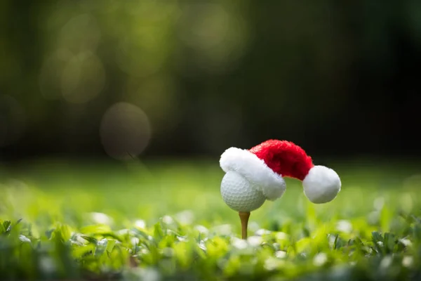Festive-looking golf ball on tee with Santa Claus\' hat on top for holiday season on golf course background