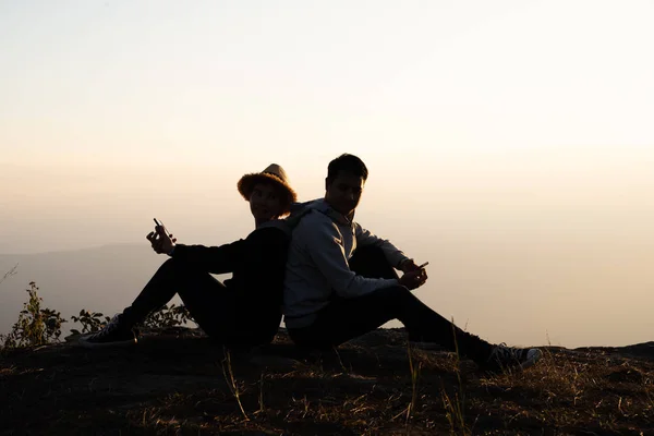 Silhouette of a couple sitting back to back using smart phones in natural surrounding