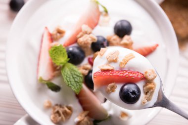 Taze meyve ve granola ile düz yoğurt üst görünümü kaşık ve kase masada üstüne
