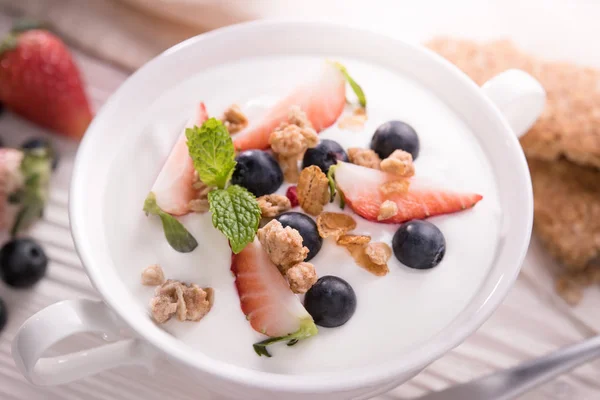 Top view of plain yogurt with fresh fruits and granola on top in bowl on the table