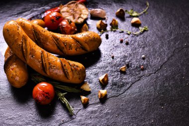 Izgara sosis ve siyah taş arka plan üzerinde çeşitli sebzeler