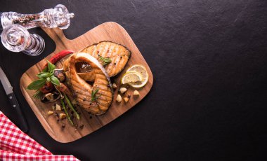 Siyah taş arka planda kesme tahtasında baharat ve çeşitli sebzeler ile ızgara somon balığı