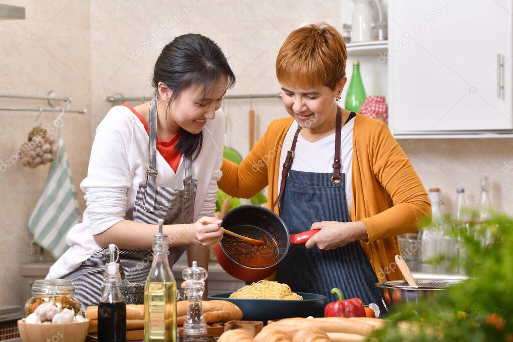 Loving Asian family of mother and daughter cooking in kitchen making healthy food together feeling fun