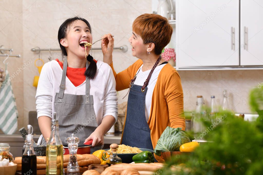 Loving Asian family of mother and daughter cooking in kitchen making healthy food together feeling fun