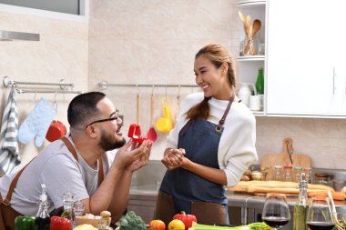Asyalı bir adam elinde yüzükle kırmızı bir kutu tutuyor. Mutfakta kız arkadaşına evlenme teklif ediyor.