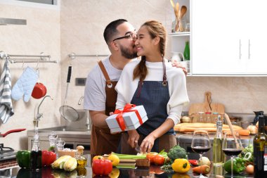 Asyalı bir kadın, mutfakta yemek pişirirken ve birlikte sağlıklı yemekler yaparken erkek arkadaşının hediyesine şaşırınca mutlu olur.