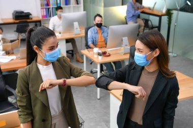 Asyalı kadınları dirsekleriyle selamlıyor ve yüz maskeleri takıyor. Yeni normal ofiste çalışıyor ve Corona virüsü covid-19 salgını sırasında sosyal mesafeler çiziyor.