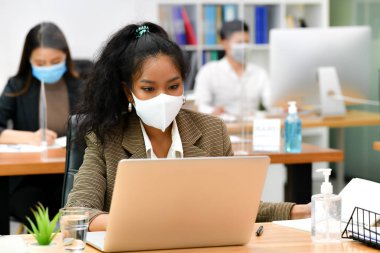 Yüz maskesi takan Asyalı kadın ofis çalışanı portresi yeni normal ofiste çalışıyor ve Corona virüsü covid-19 salgını sırasında sosyal uzaklık yapıyor.