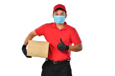 Kırmızı üniformalı, tıbbi maskeli, koruyucu eldivenli mutlu Asyalı teslimatçı beyaz arka planda karton kutu taşıyor. Teslimatçı çocuk paket teslimatı yapıyor. Güvenli teslimat.